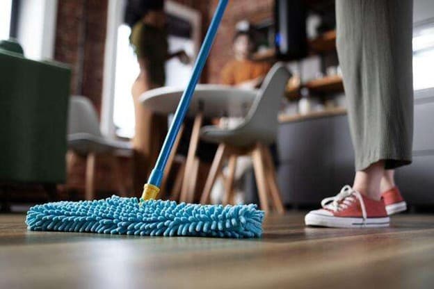 A close-up of a person mopping a wood floor, demonstrating essential flooring maintenance tips for Tampa homeowners to keep surfaces clean.