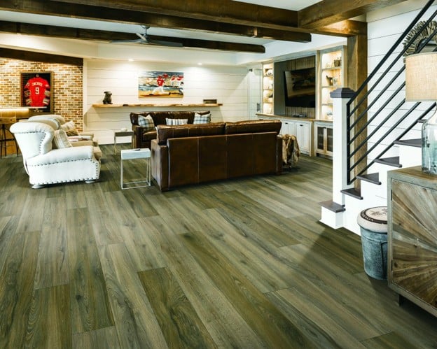 A spacious basement living room featuring wide-plank, wood-look vinyl flooring, exposed wooden beams, and leather sofas.