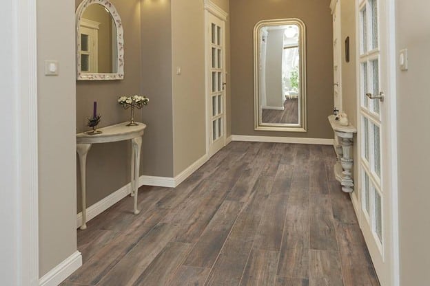 An elegant hallway with dark, wood-look plank flooring, cream walls, and a large arched floor mirror.